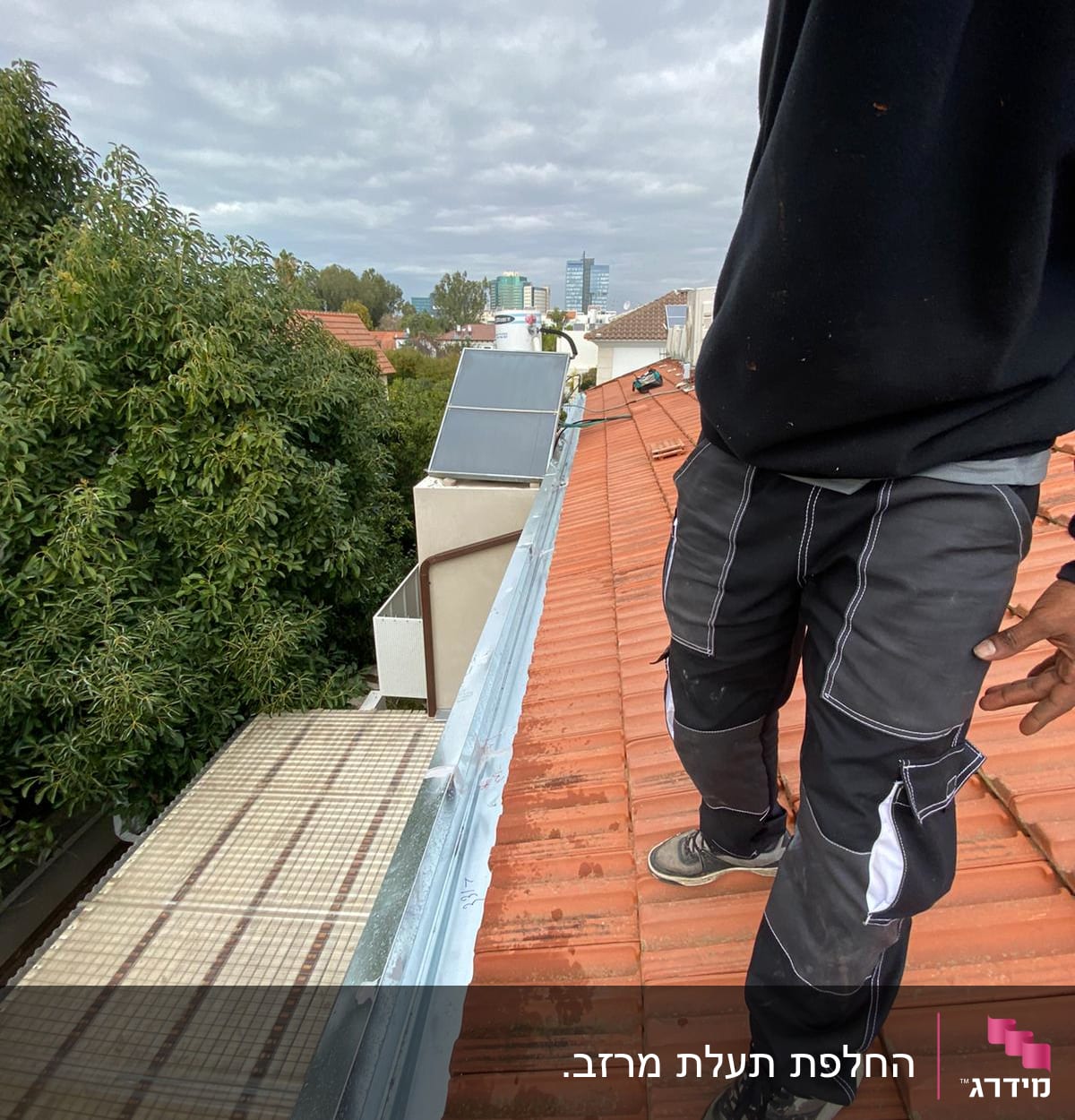 אדם עומד על גג רעפים עם מרזב מתכת